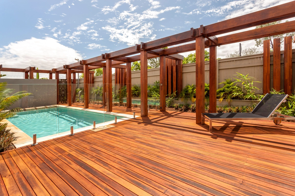 Terrasse en bois avec pergola moderne entourant une piscine, aménagée par MABO pour créer un espace de vie extérieur convivial et élégant.