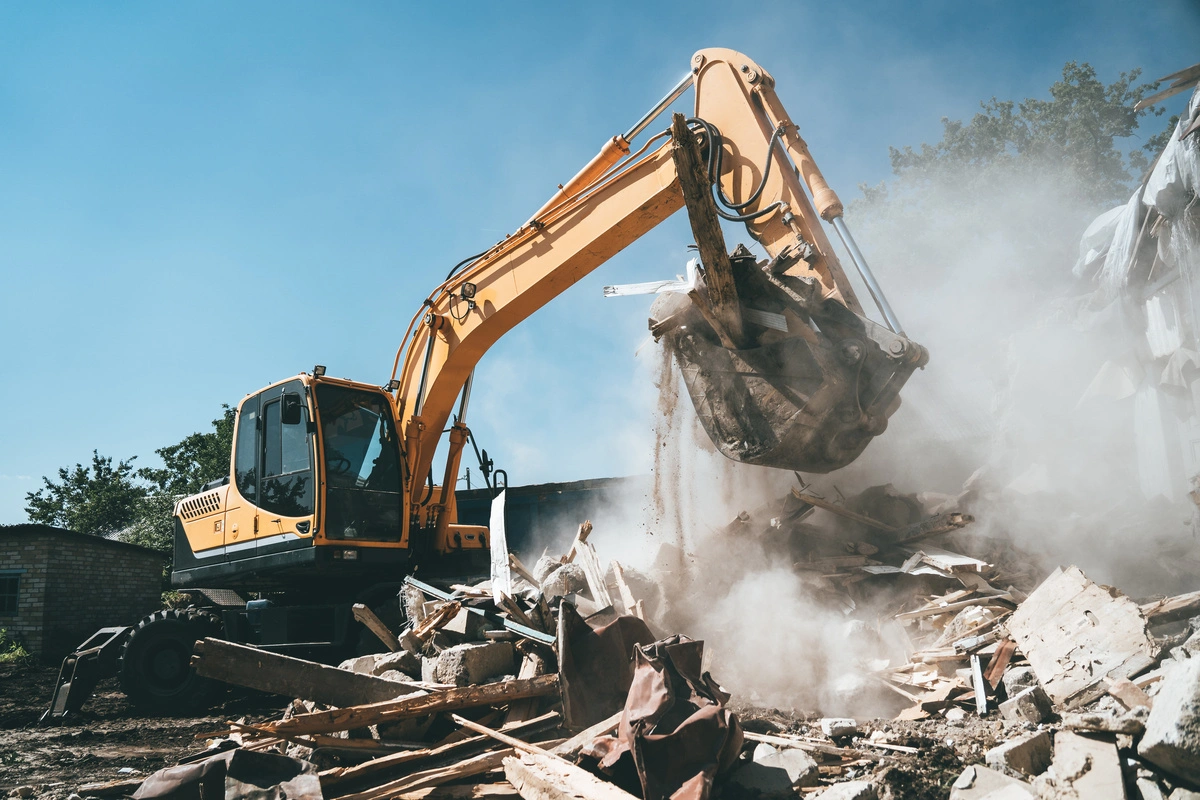 Pelleteuse en action lors d'une démolition de bâtiment, soulevant des débris de construction sur un chantier de travaux publics.