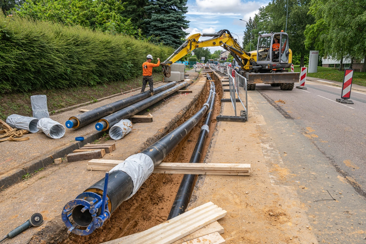 Travaux de voirie avec installation de grandes canalisations sous une route, mettant en scène des ouvriers et des engins de chantier en action.