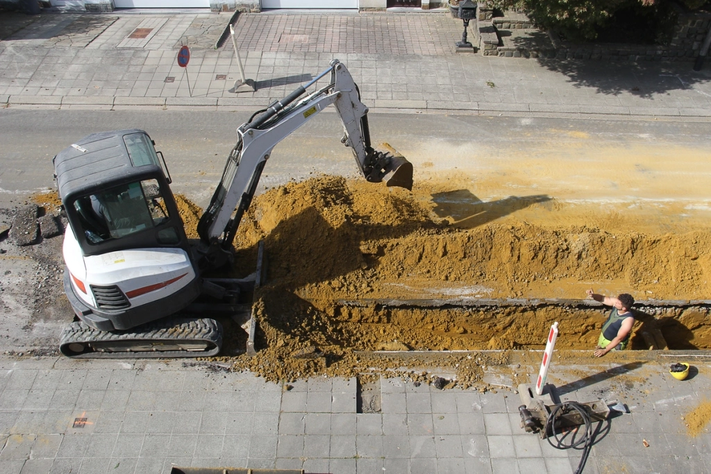 Travaux de voirie avec une pelleteuse creusant une tranchée sur une route urbaine.